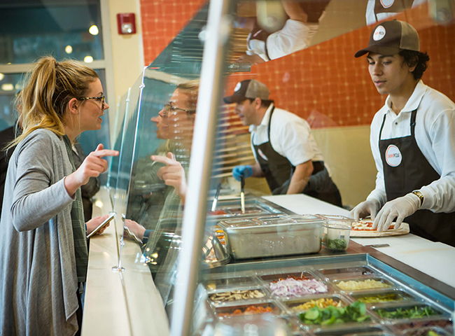 Woman at Pizza Counter Pointing to The Ingredients She Wants on Her Pizza